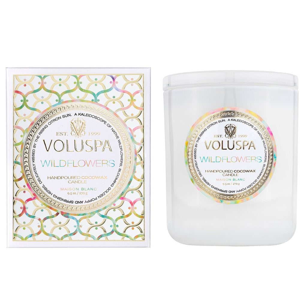 The Voluspa - Wildflowers Classic 9.5oz Candle from the Maison Blanc collection comes in a decorative box and white jar, hand-poured with clean-burning coconut wax blend featuring a colorful pattern with gold accents, highlighting the scent of native wildflowers.