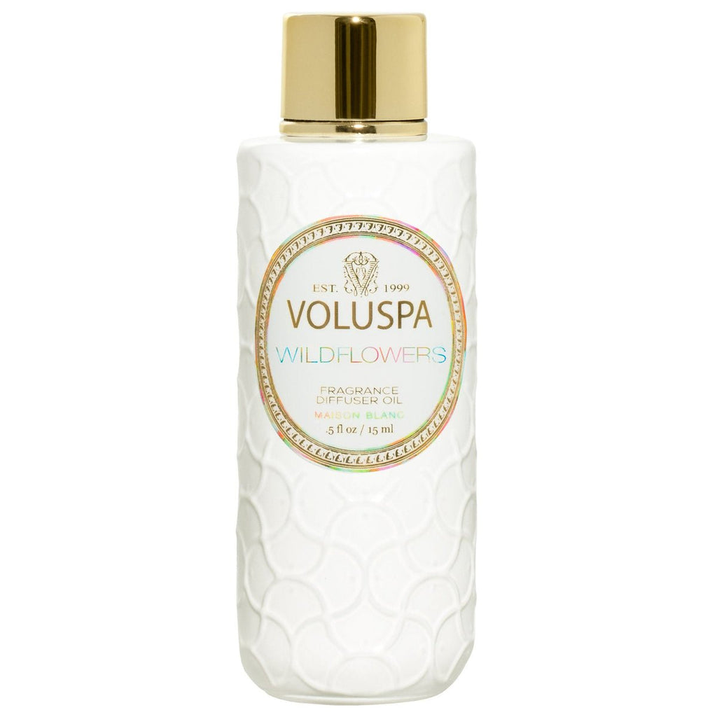 A white textured Voluspa Wildflowers Fragrance Diffuser Oil bottle, adorned with a shiny gold cap and an oval label with gold accents, elegantly highlights product details celebrating Native Wildflowers and hints of Golden Poppy.