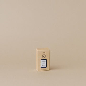 A small beige box with blue and gold labeling stands on a plain beige background, giving off a subtle lavender scent. The Votivo - Pura Refills box has a minimalist design, featuring Votivo branding at the top.