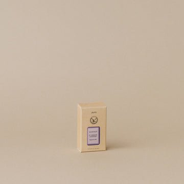 A small beige rectangular box with a purple label is centered on a light brown background. The label, featuring dark ink text and logo, suggests the calming aroma of Votivo - Pura Refills in lavender—a perfect addition to your self-care ritual.