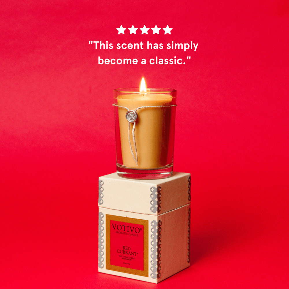 A lit Votivo - Red Currant Aromatic 6.8oz Candle in a glass jar rests on its box against a red background, with five stars above and the text: This Red Currant Fragrance by Votivo has simply become a classic.