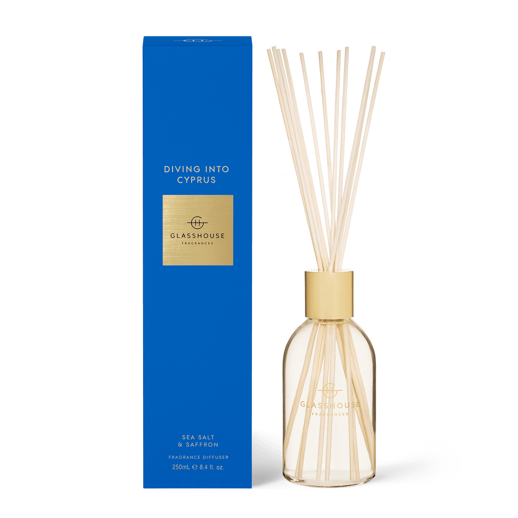 A clear, gold-toned diffuser branded Glasshouse Fragrances sits before a tall blue box labeled Diving into Cyprus, blending sea salt and saffron aromas for an exquisite experience.