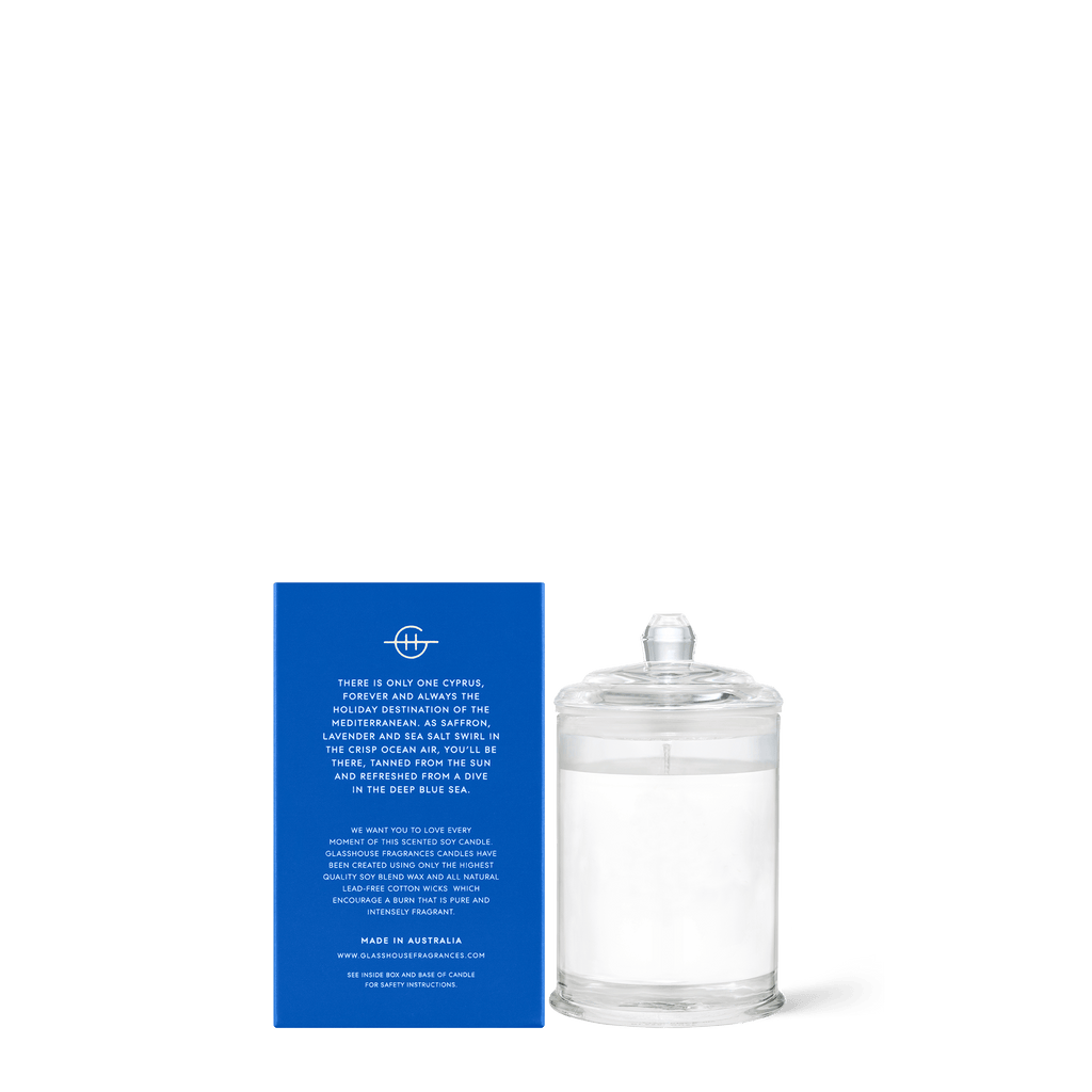 A Glasshouse Fragrances Diving into Cyprus mini soy candle in a clear jar with a lid is next to its blue box, featuring white text on freesia, lavender, lime, and sea salt fragrance. Made in Australia.