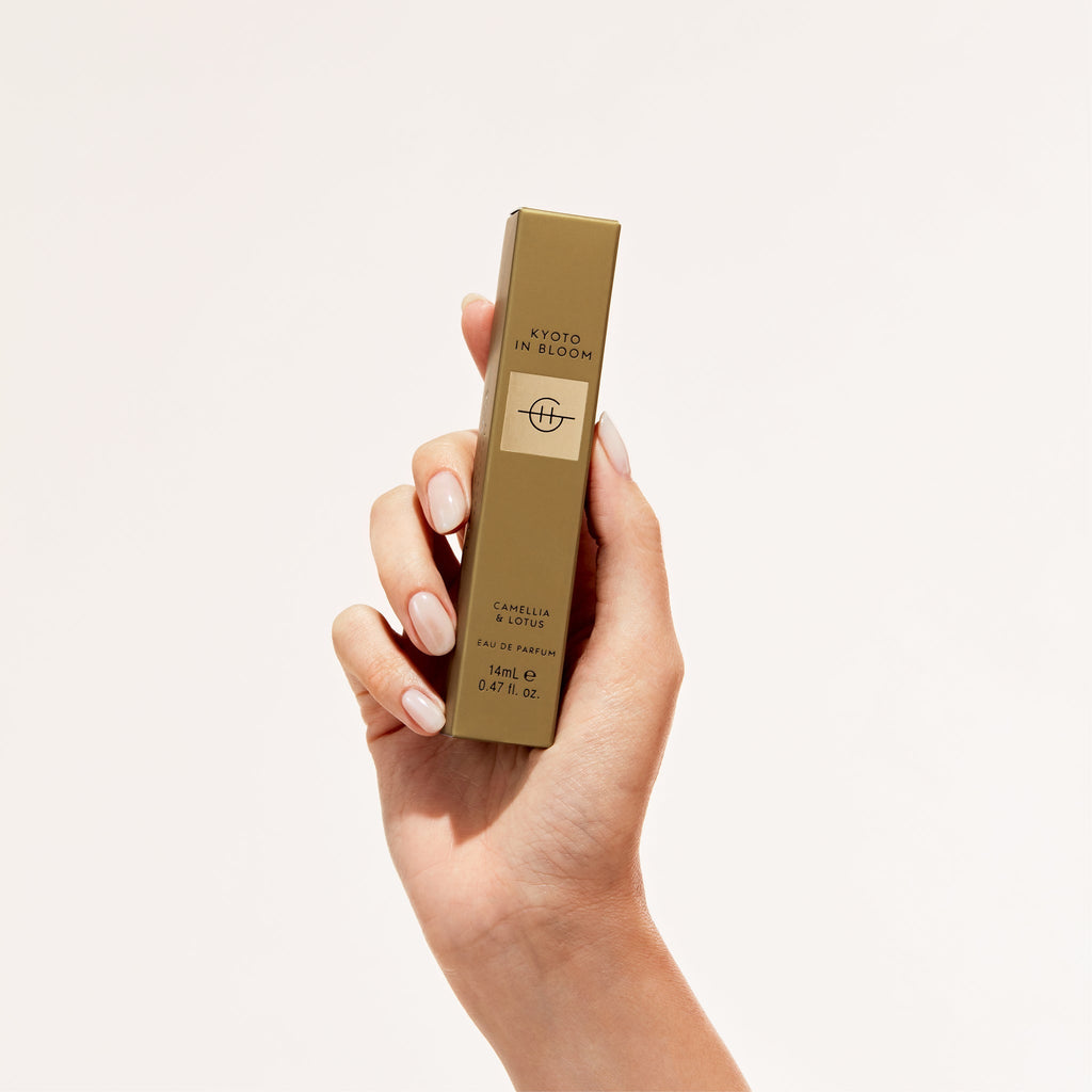 A hand with light pink nails holds the Glasshouse Fragrances Eau de Parfum 14ml – Kyoto In Bloom, against a plain light background. The gold rectangular box features Kyoto in Bloom and contains an exquisite white floral scent.