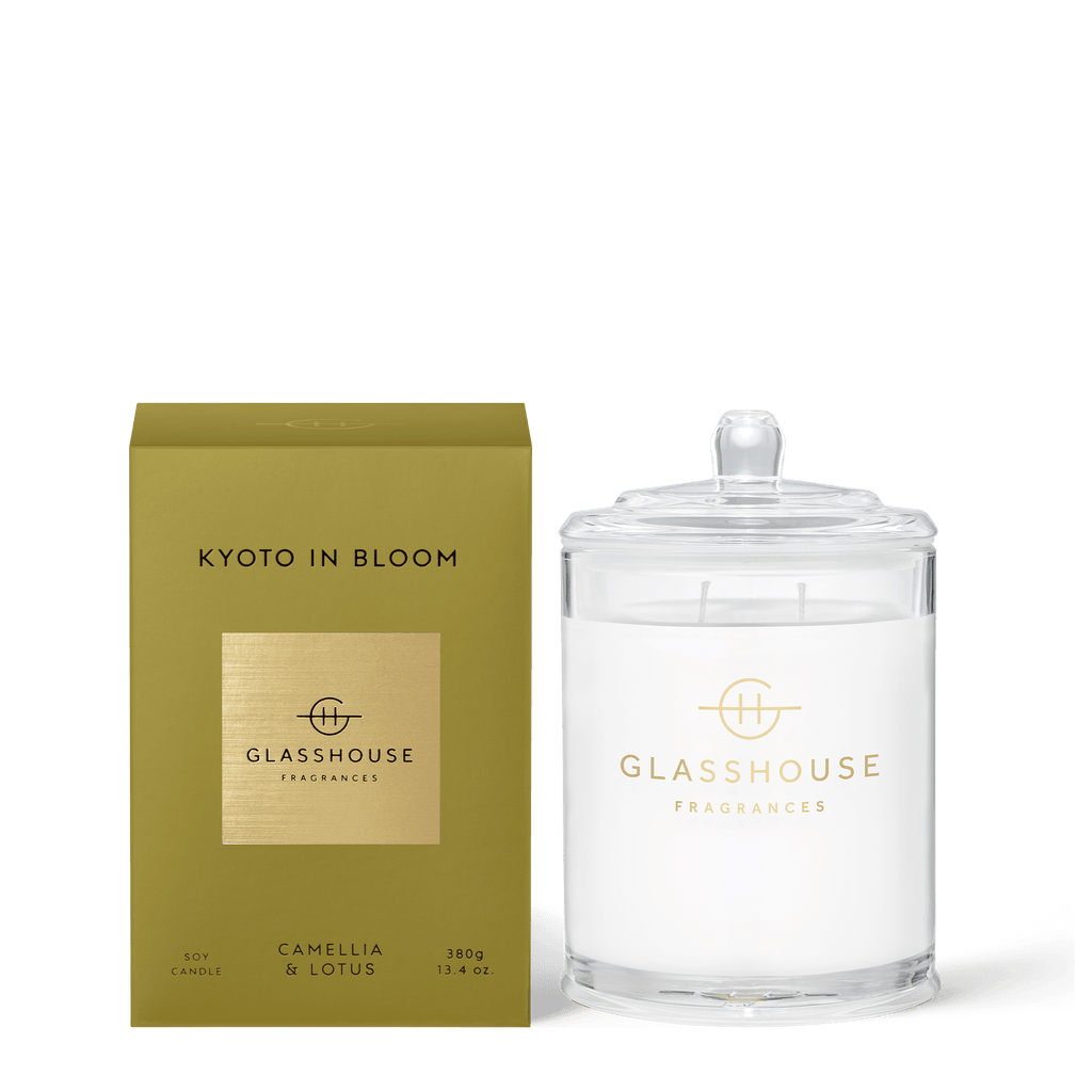 A gold Kyoto in Bloom box sits beside a lidded Glasshouse Fragrances 13.4oz soy candle jar. Both display the Glasshouse Fragrances logo and feature the Camellia & Lotus scent.