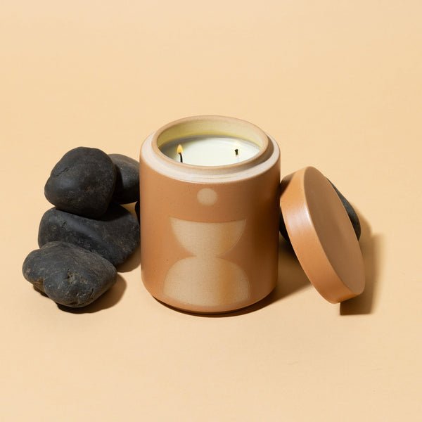 The Paddywax Form Wild Fig + Vetiver 12oz candle features a tan ceramic jar with a geometric lid, shown on a beige surface by smooth black stones—an elegant modern accent from Paddywax for your space.