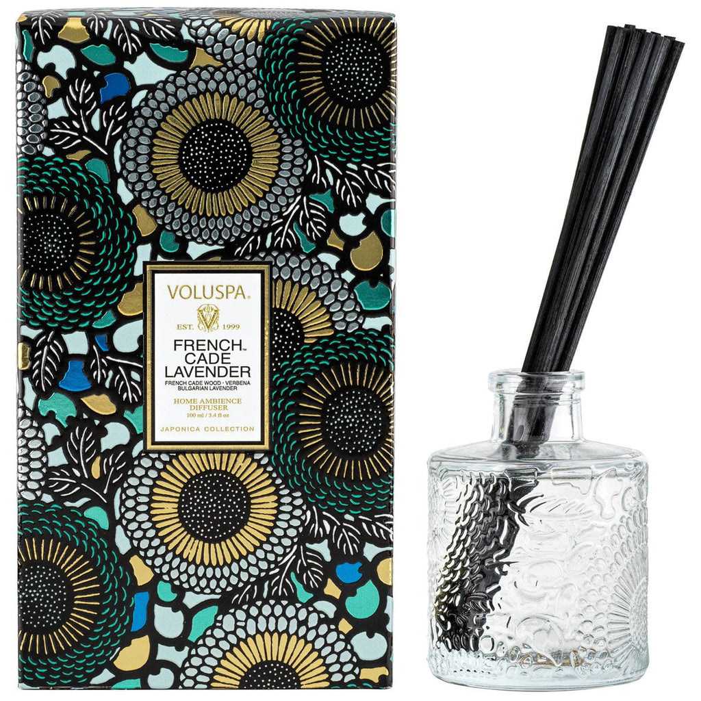 The Voluspa French Cade Lavender 3.4oz Reed Diffuser set includes a floral-patterned box with black, green, and gold accents. A clear glass bottle with black reeds releases soothing scents, capturing serenity for your space.