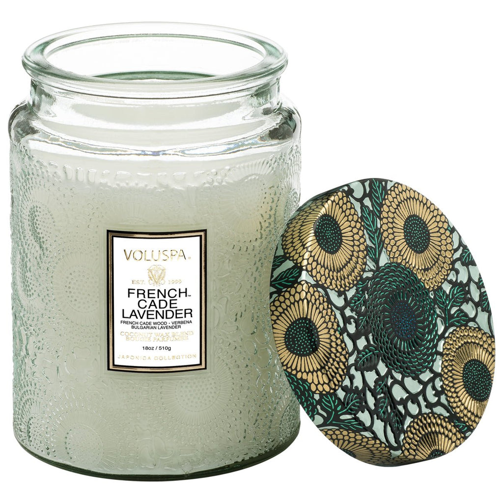 A textured large glass candle labeled Voluspa French Cade Lavender is crafted with coconut wax. Its lid displays sunflower patterns in green, yellow, and black and rests against the Voluspa - French Cade Lavender Large Jar 18oz Candle.