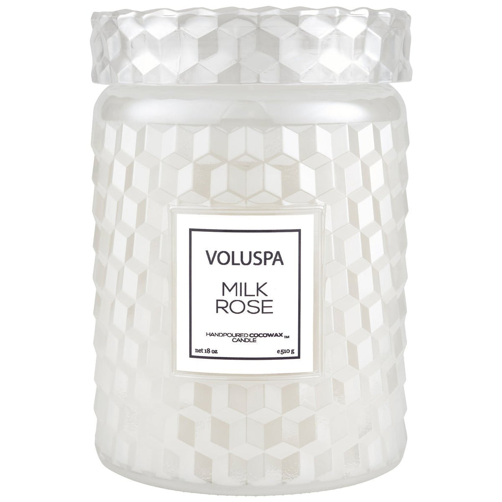 The Voluspa - Milk Rose Large 18oz Jar Candle comes in a clear jar with a geometric pattern and label. It contains white coconut wax blended with Bulgarian rose and is topped with a textured lid.