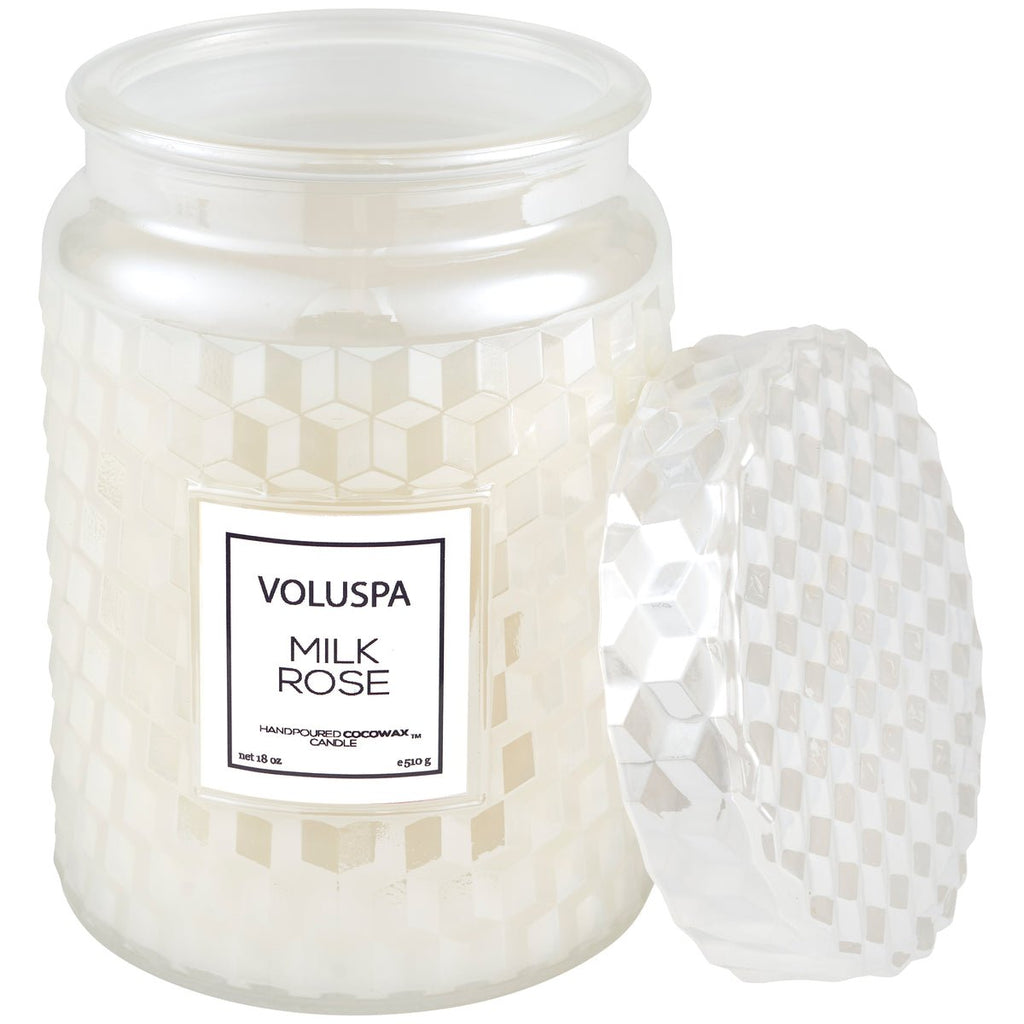 An 18oz Voluspa Milk Rose candle in a white jar with a geometric pattern and textured lid is open, revealing its coconut wax and Bulgarian rose scent.