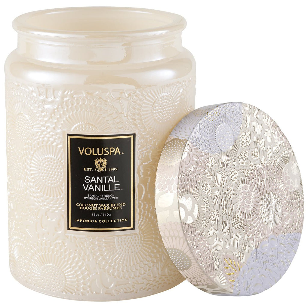 The Voluspa - Santal Vanille Large Jar 18oz Candle from the Japonica Collection features an elegant cream-colored jar with intricate floral patterns, a shiny finish, and an open matching lid. Hand-poured with a luxurious coconut wax blend, it adds elegance to any space.